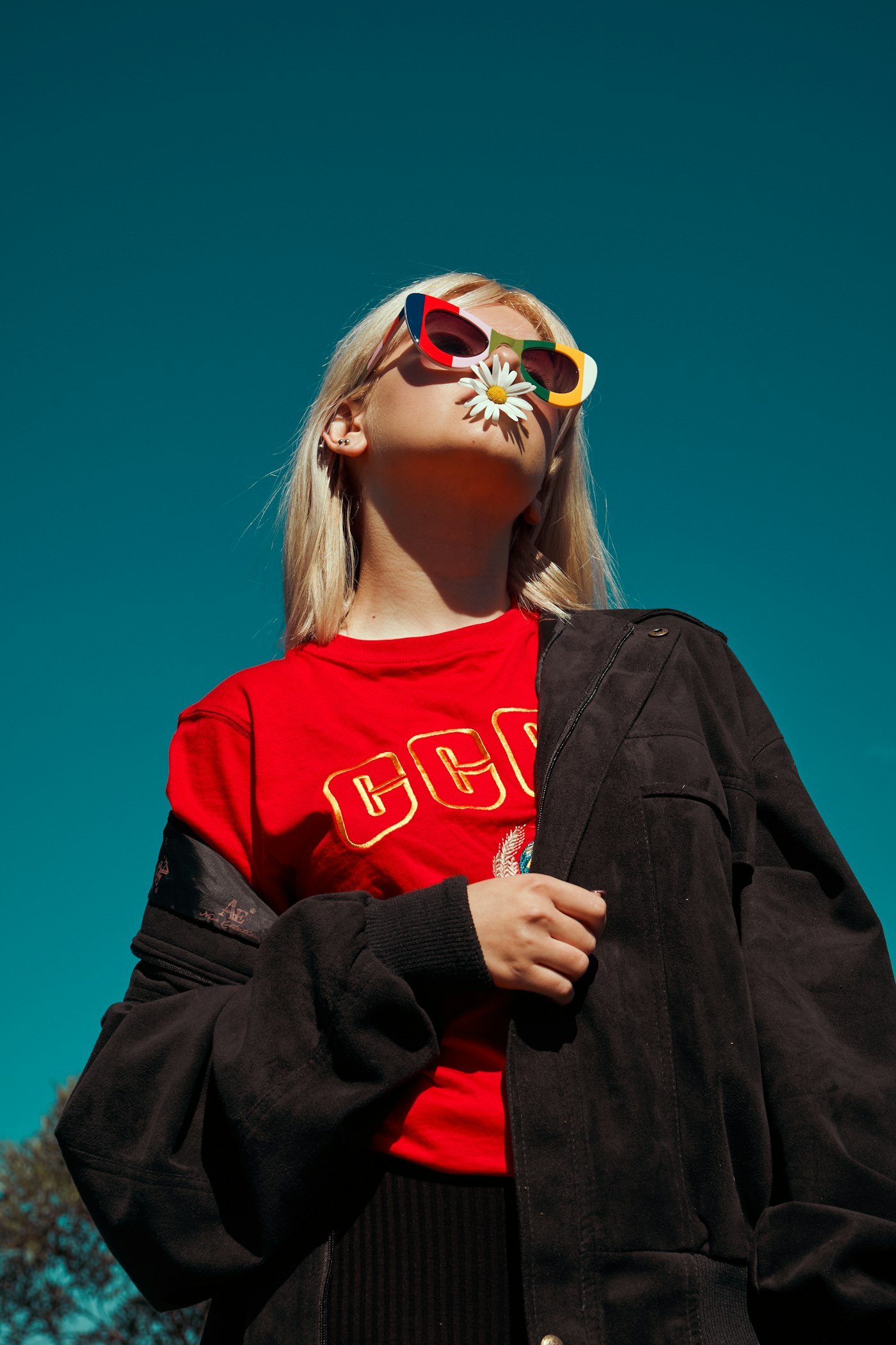 Woman in red top and oversized sunglasses against a deep teal backdrop