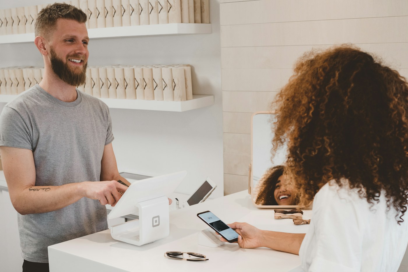 Customer paying by phone at a shop counter served by a smiling assistant